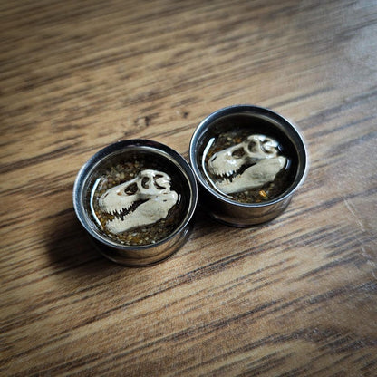plug earrings with a 3d dinosaur skull insert on a wooden background