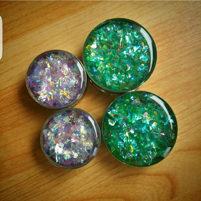 Four glittery green and purple plug earrings on a wooden surface