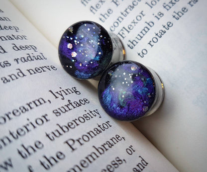Hand painted galaxy plug earrings against a book backdrop
