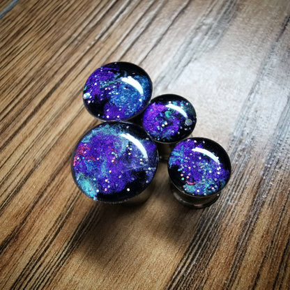 Galaxy style plug earrings against a wooden backdrop