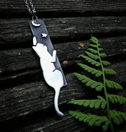 Necklace with a cat-shaped pendant on a wooden surface with a fern leaf.