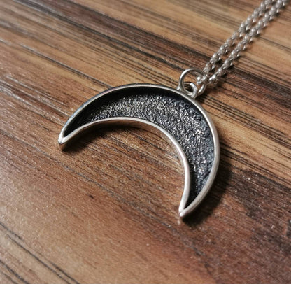 Silver crescent moon necklace on a wooden surface