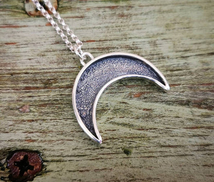 Silver crescent moon necklace on a wooden surface