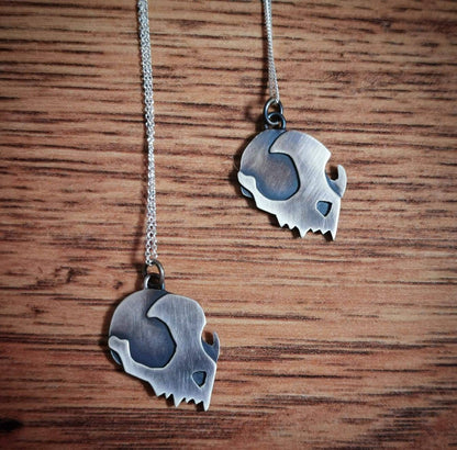 Two silver skull-shaped pendants on a chain against a wooden background