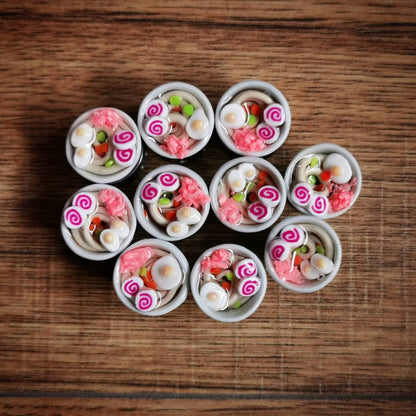 Small white bowls plug earrings filled with colorful ramen themes on a wooden surface