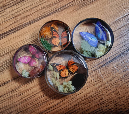 Four round plug earrings with butterflies and flowers on a wooden surface