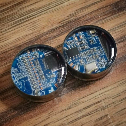 Our blue circuit board plugs on a wood beckground, they show the stainless steel plug with a bright blue real circuit board inlay made using real circuit boards. These are in bright blue, we also have green available