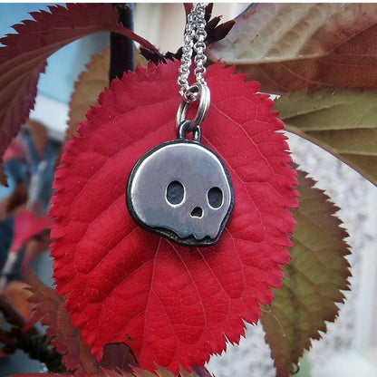 Oxidised silver skull mini skull pendant shown against a red leaf 