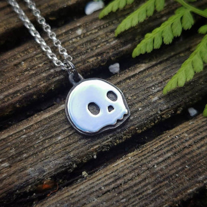 Skull-shaped pendant on a chain lying on wooden surface with green leaves