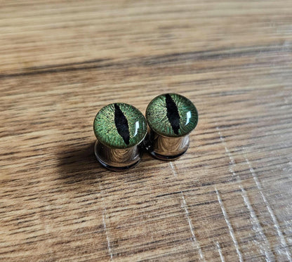 Pair of green cat eye-shaped plug earrings on a wooden surface