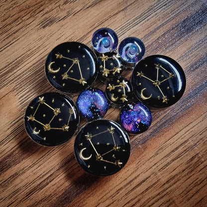 Set of celestial-themed plug earrings on a wooden surface