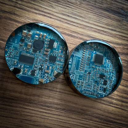 Two circular electronic components plug earrings on a wooden surface