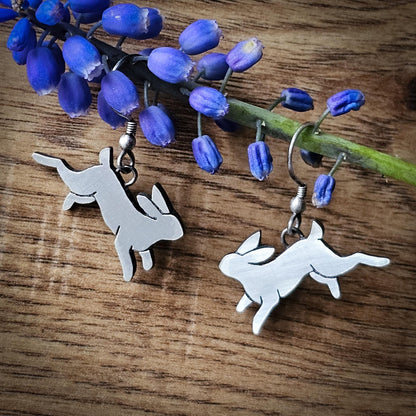Silver rabbit-shaped earrings on a wooden surface with blue flowers.