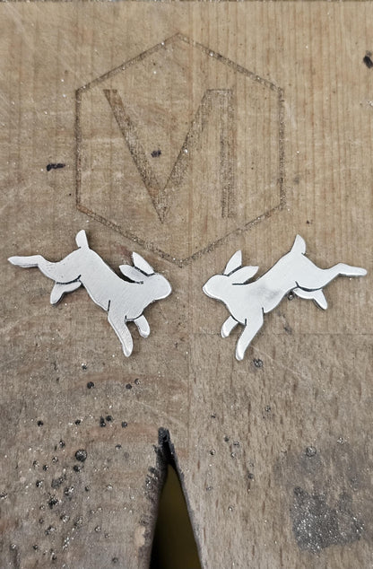 Metallic rabbit-shaped earrings on a textured jewellers benchpeg background