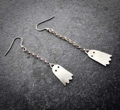 Pair of silver ghost-shaped earrings on a dark gray surface