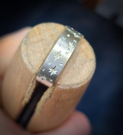 Silver ring with star patterns held against a wooden block