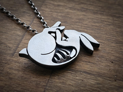 Silver necklace with a detailed rabbit pendant on a wooden surface, the rabbit is silver toned with a protruding metal ribcage, and is darkly oxidised 