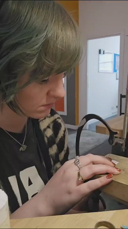 Short video showing the maker of the jewellery pieces sawing out the jewellery at a work bench before showing an in progress shot and finally a shot of a silver toned rabbit pendant with a protruding ribcage